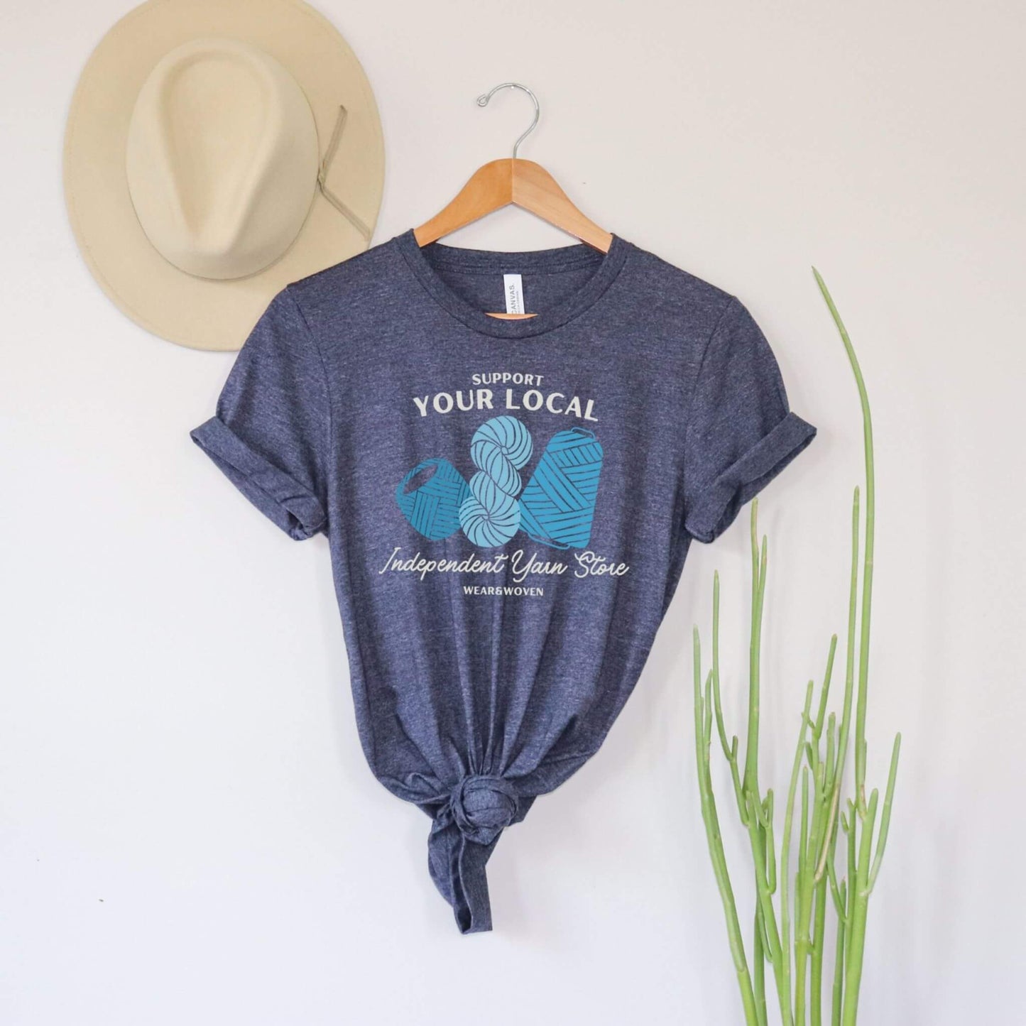 support your local independent yarn store dark heather blue t-shirt. shirt has three images of yarn in different shades of blue