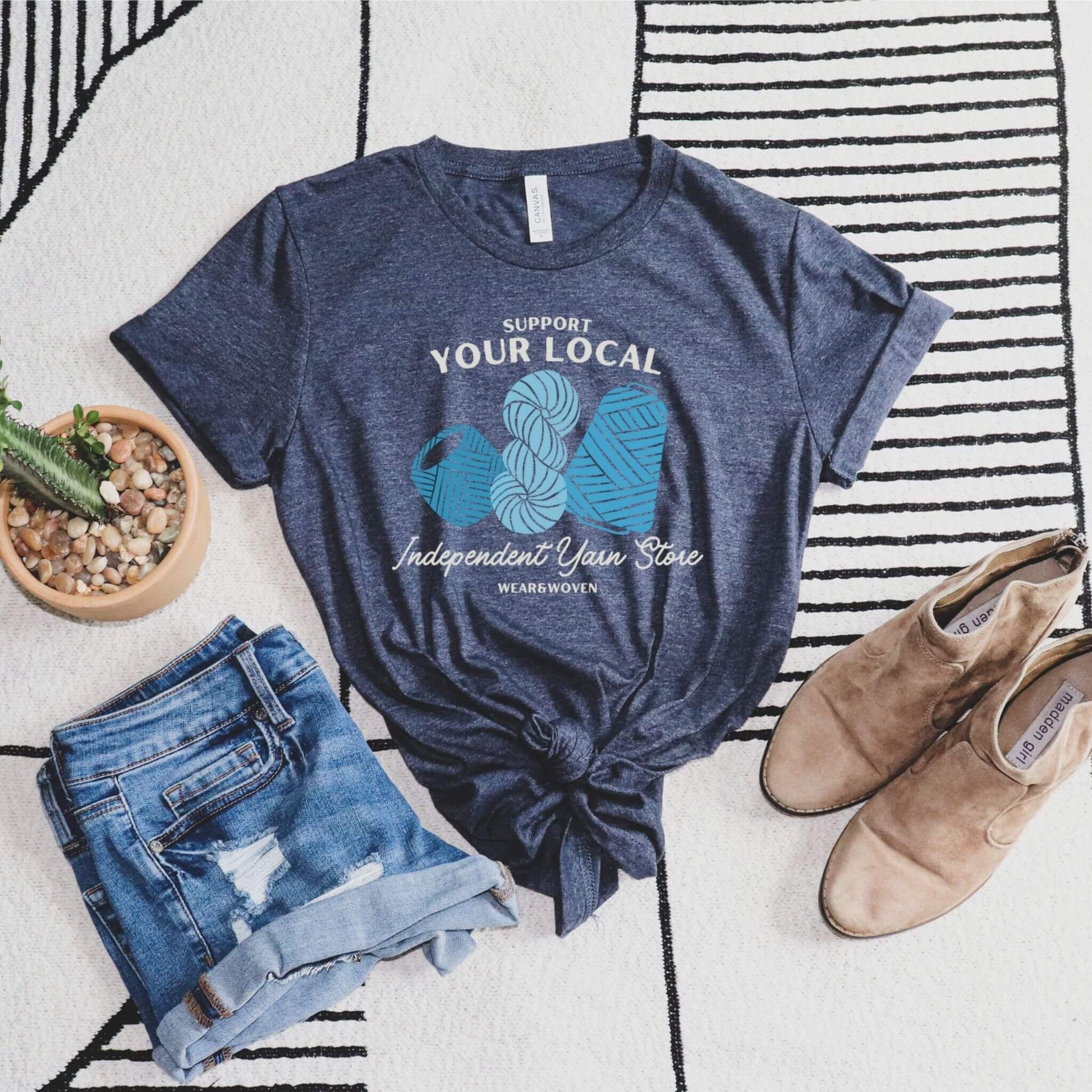support your local independent yarn store dark heather blue t-shirt. shirt has three images of yarn in different shades of blue